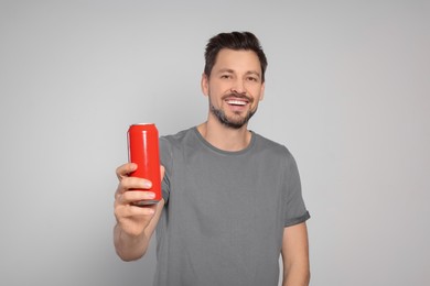 Photo of Happy man holding red tin can with beverage on light grey background