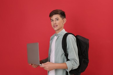 Photo of Teenage student with backpack and laptop on red background