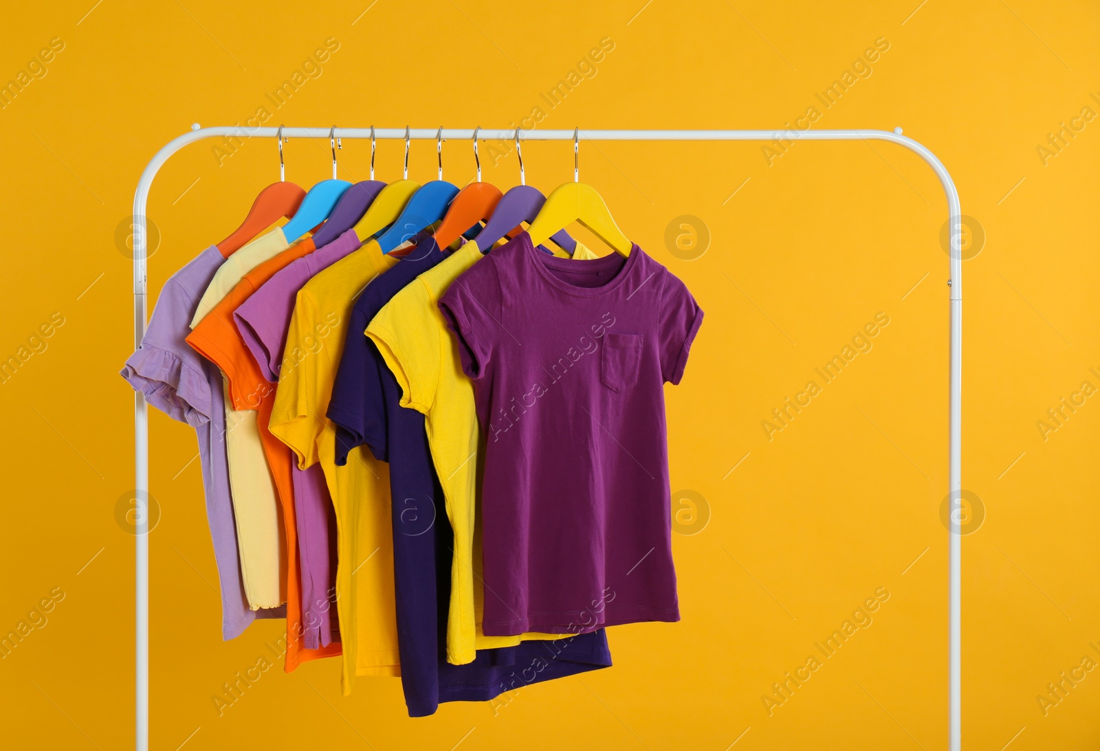 Photo of Rack with stylish children clothes on yellow background