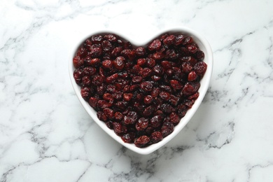Photo of Heart shaped bowl with cranberries on marble table, top view. Dried fruit as healthy snack