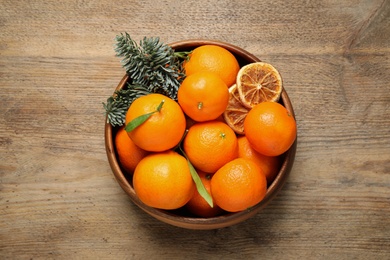 Photo of Fresh tangerines with fir tree branches in bowl on wooden table, top view. Christmas atmosphere