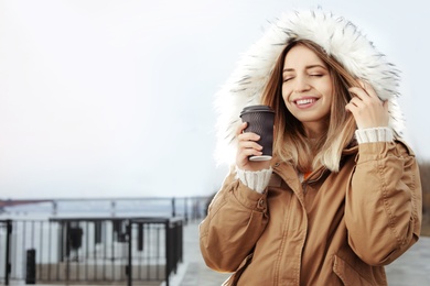 Photo of Young woman with cup of coffee walking outdoors. Space for text