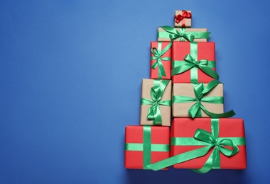 Photo of Christmas tree shape of gift boxes on blue background, flat lay. Space for text