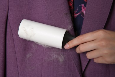 Woman removing hair from purple jacket with lint roller, closeup