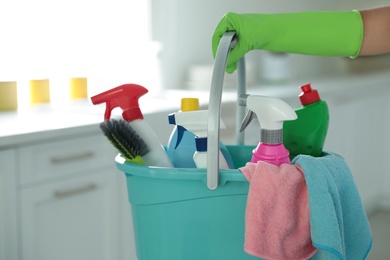 Photo of Woman holding bucket with cleaning supplies in kitchen, closeup