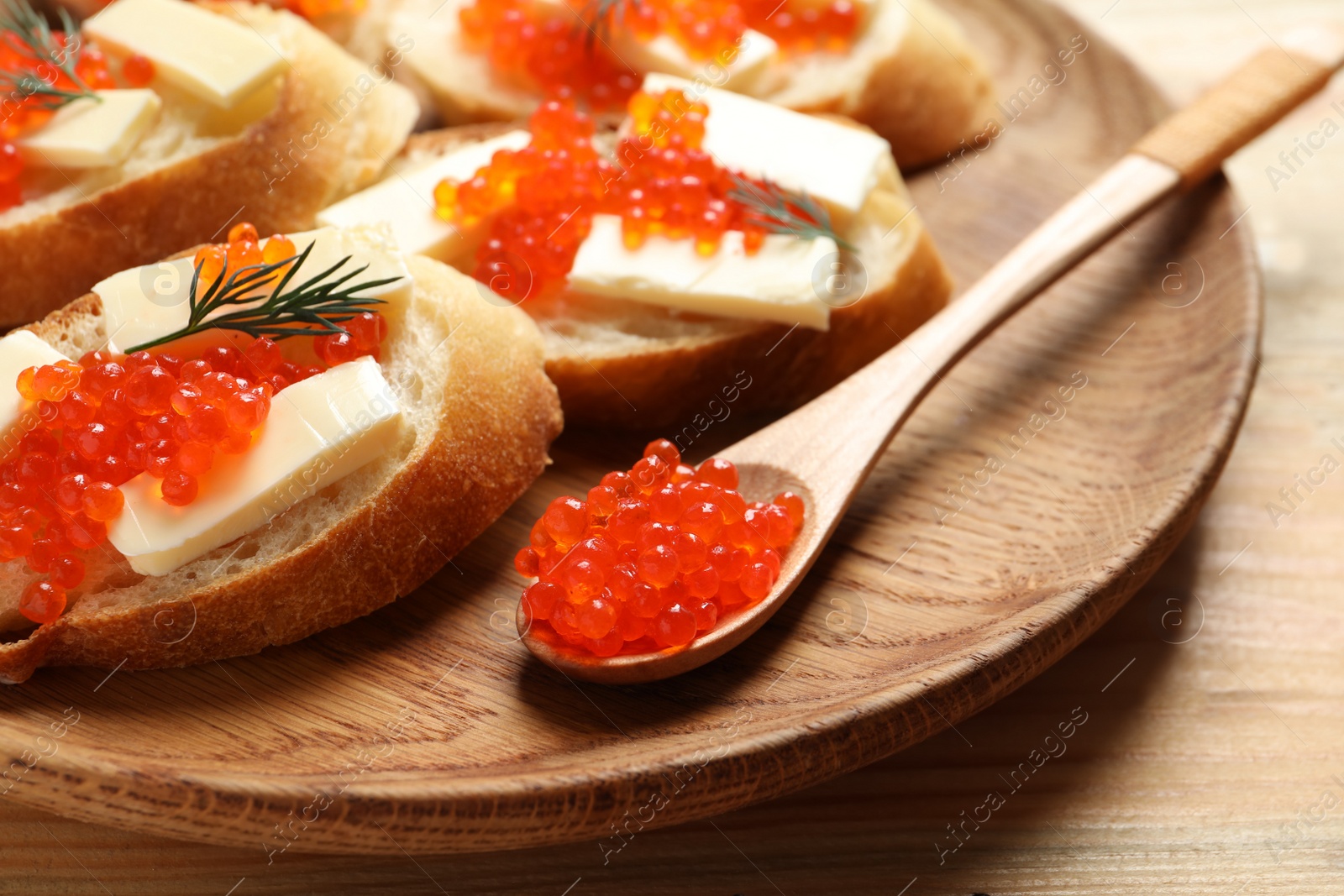 Photo of Delicious sandwiches and spoon with red caviar on wooden plate, closeup