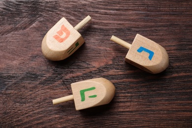 Photo of Hanukkah traditional dreidels with letters He, Pe and Nun on wooden table, flat lay
