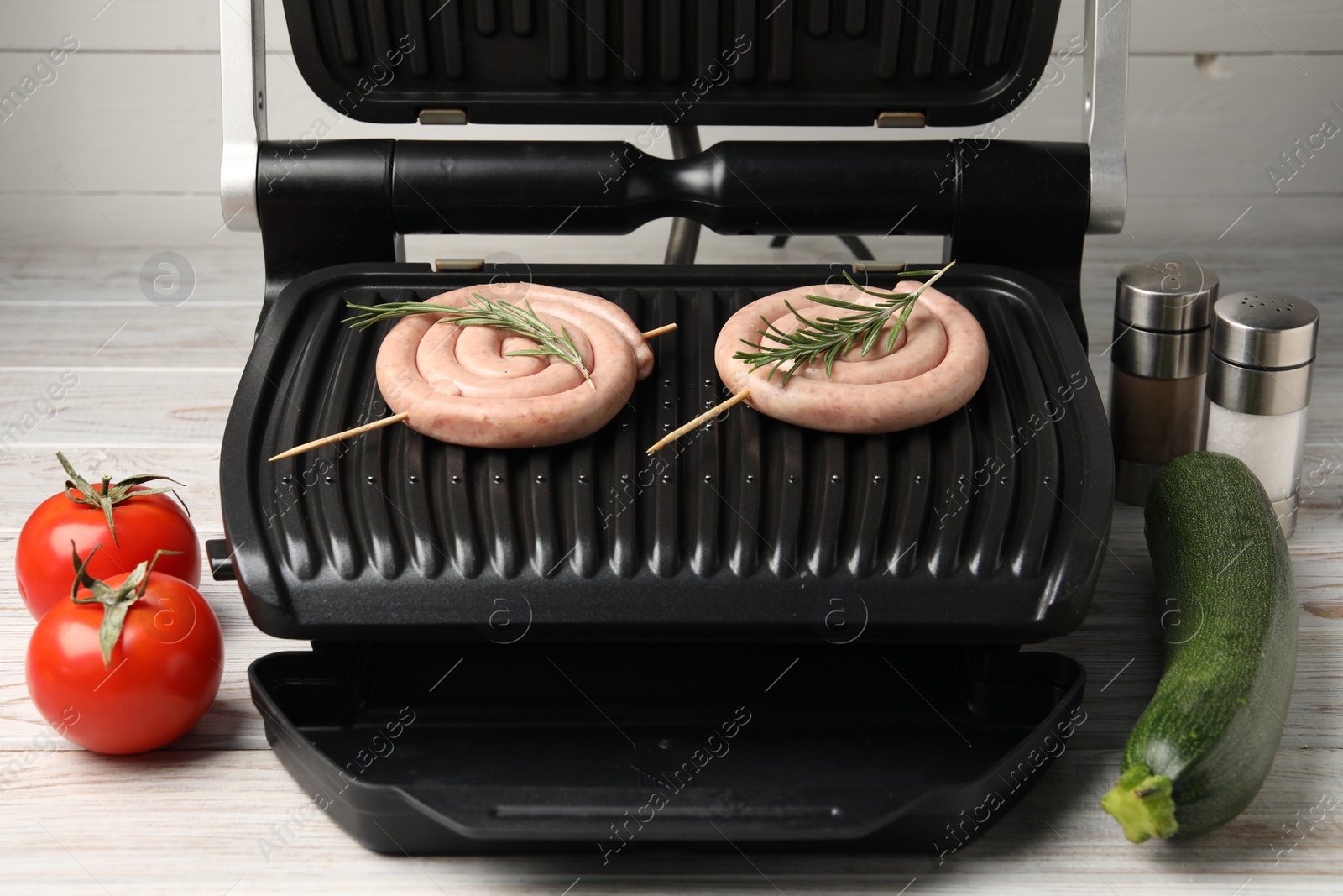 Photo of Electric grill with homemade sausages, rosemary, vegetables and spices on wooden table