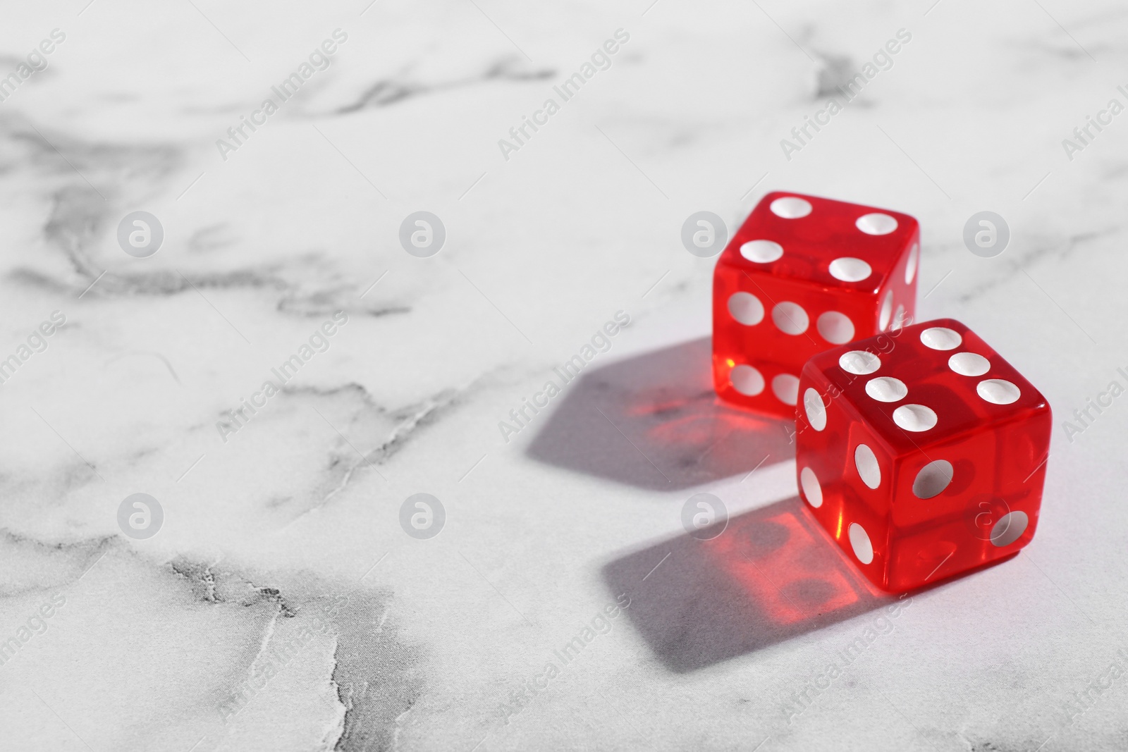 Photo of Two red game dices on white marble table, closeup. Space for text