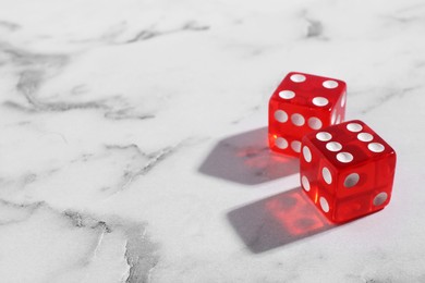 Two red game dices on white marble table, closeup. Space for text