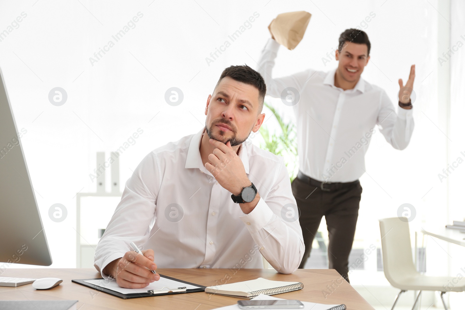 Photo of Man popping paper bag behind his colleague in office. April fool's day