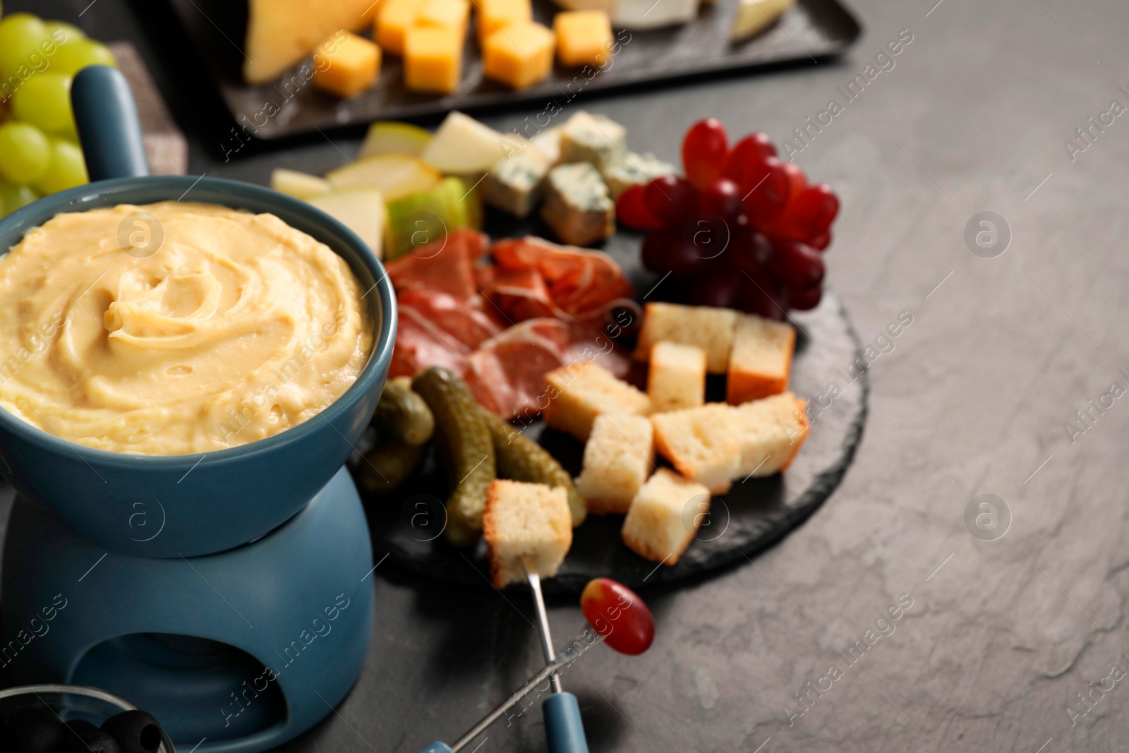 Photo of Fondue with tasty melted cheese, forks and different snacks on black table