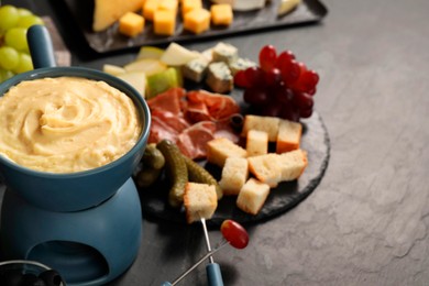 Photo of Fondue with tasty melted cheese, forks and different snacks on black table