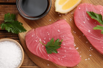 Photo of Raw tuna fillets with parsley and spices on wooden table, flat lay