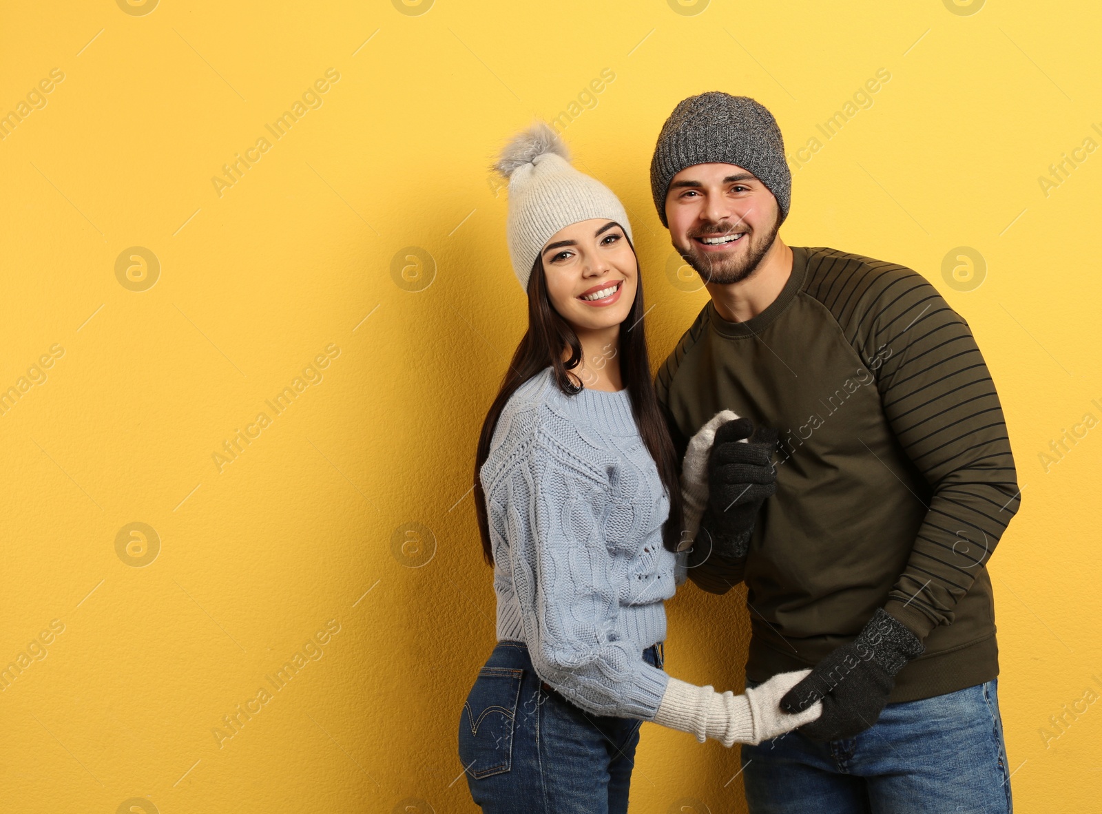 Photo of Happy young couple in warm clothes on yellow background, space for text. Winter vacation