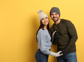 Happy young couple in warm clothes on yellow background, space for text. Winter vacation