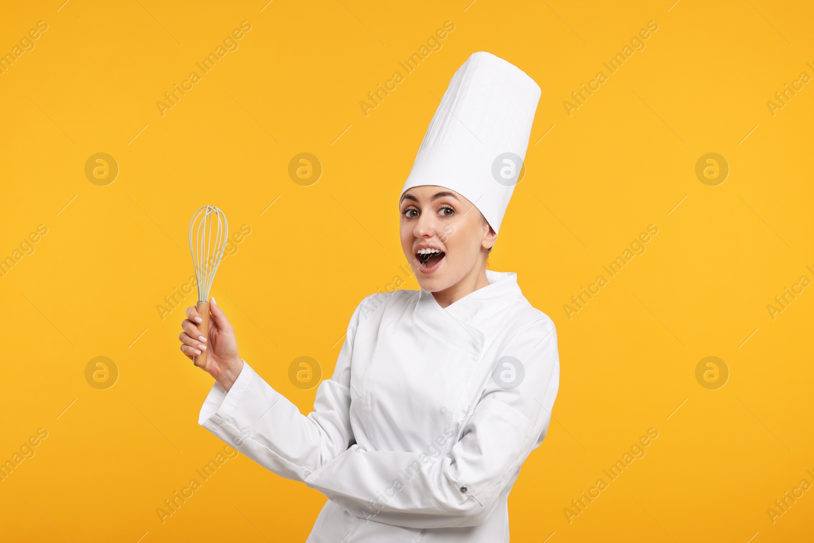 Photo of Surprised professional confectioner in uniform holding whisk on yellow background