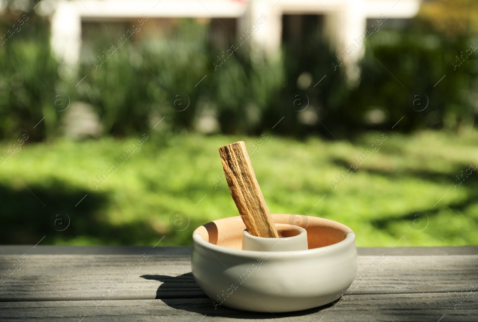 Photo of Palo santo stick in holder on wooden table outdoors