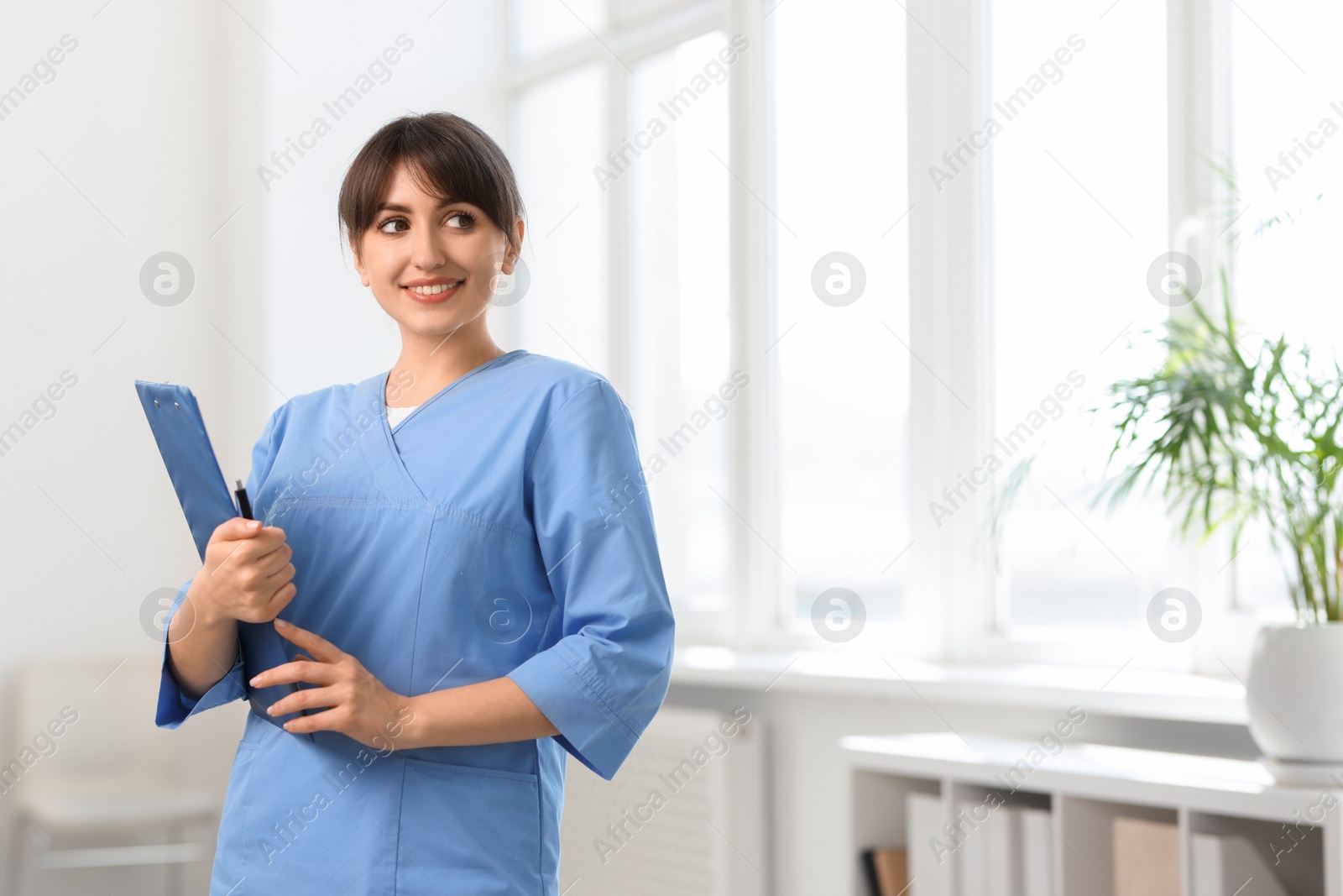 Photo of Portrait of smiling medical assistant with clipboard and pen in hospital. Space for text