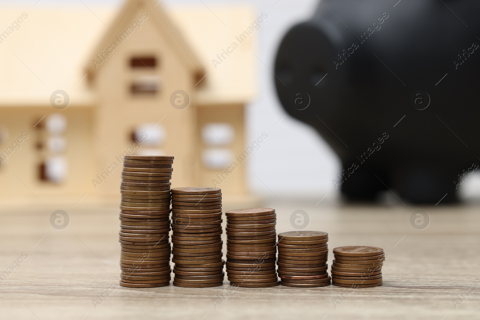 Photo of House model, piggy bank and stacked coins on wooden table, closeup