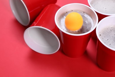 Plastic cups and ball for beer pong on red background