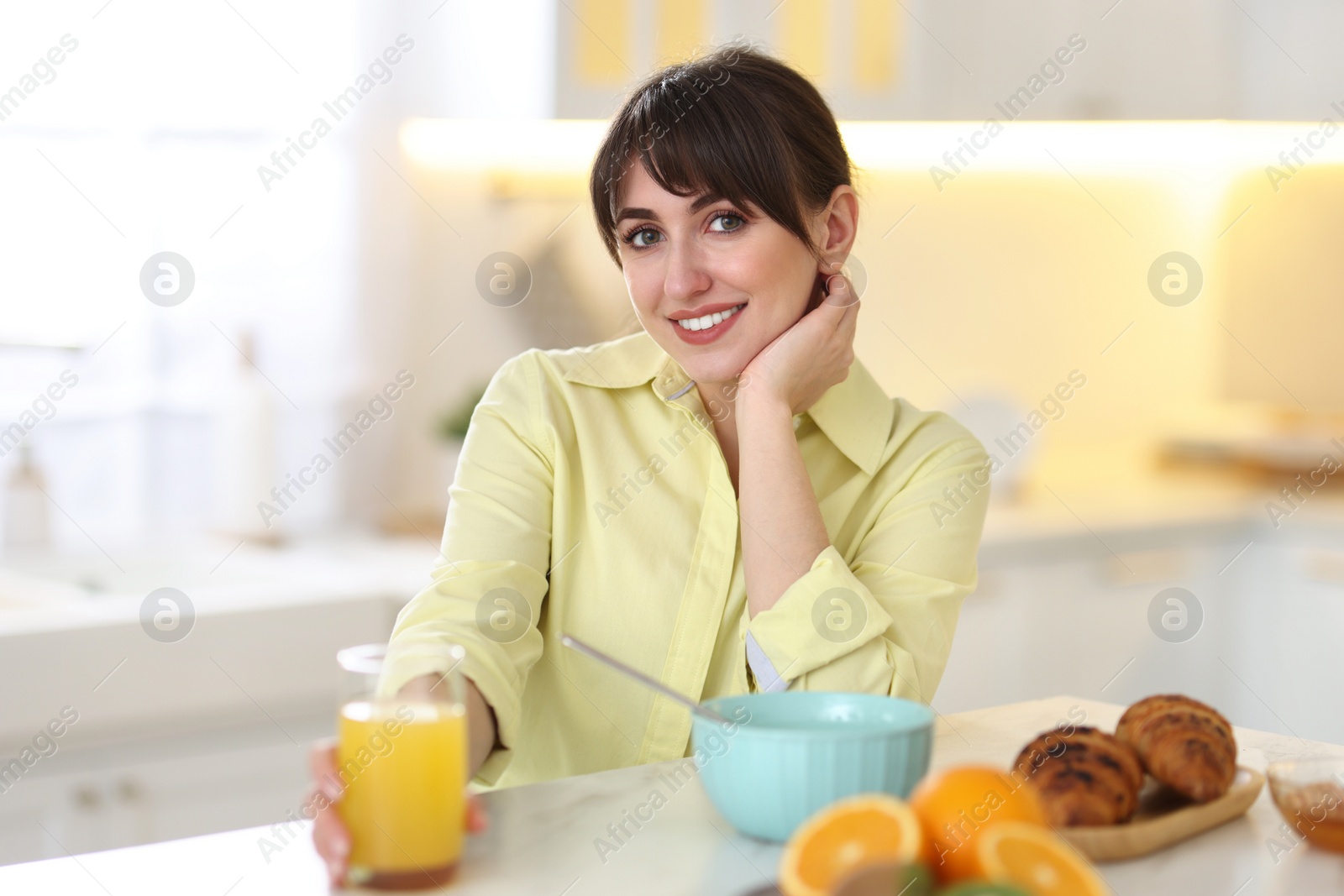 Photo of Smiling woman with glass of juice having breakfast at home