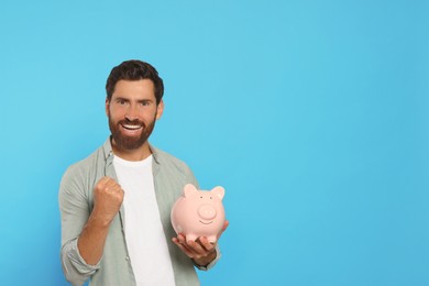 Photo of Happy man with ceramic piggy bank on light blue background, space for text