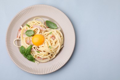 Photo of Delicious pasta Carbonara with egg yolk on light blue background, top view. Space for text