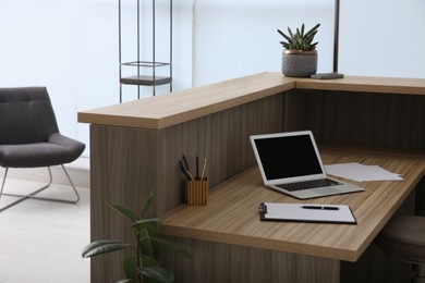 Photo of Stylish modern wooden desk with laptop indoors. Receptionist workplace