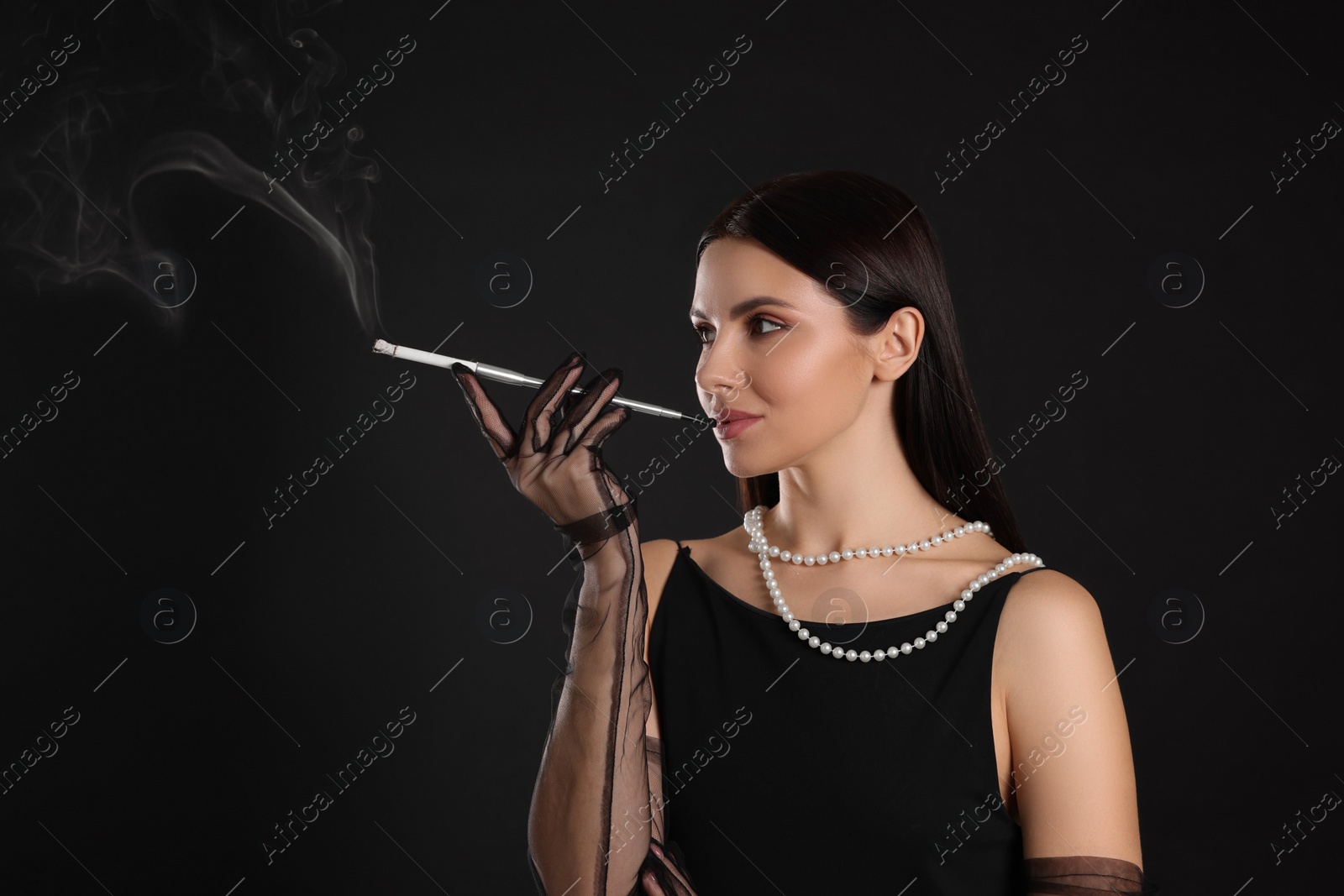 Photo of Woman using long cigarette holder for smoking on black background, space for text