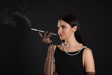 Photo of Woman using long cigarette holder for smoking on black background, space for text