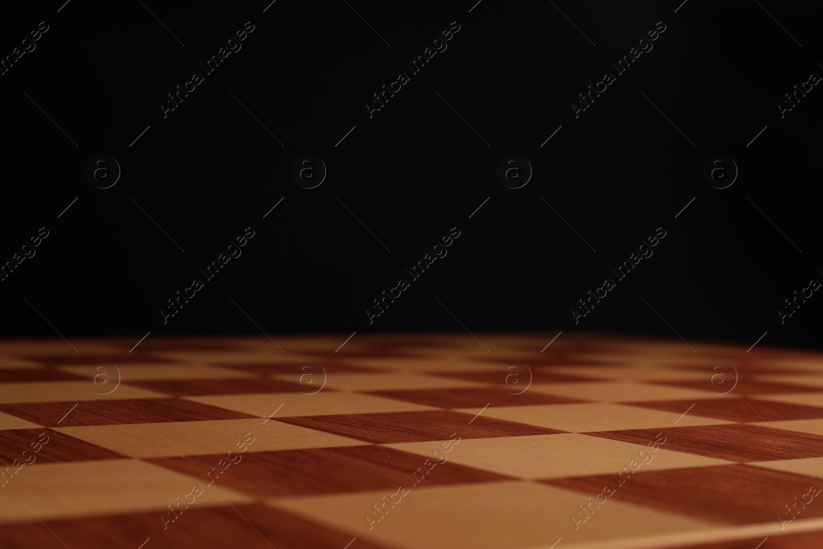 Photo of Empty wooden chess board against black background, closeup. Space for text