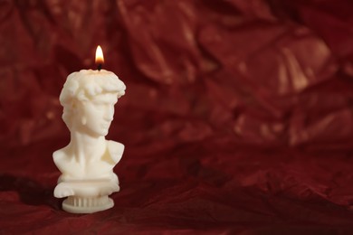 Photo of Beautiful burning David bust candle on red crumpled parchment. Space for text