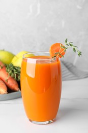 Glass with healthy carrot juice and ingredients on white table