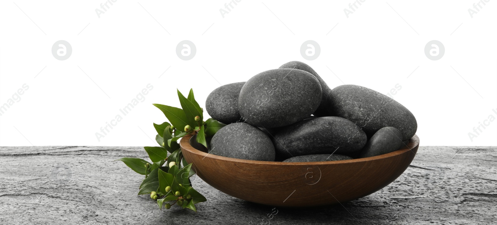 Photo of Bowl with spa stones and green branch on grey table against white background