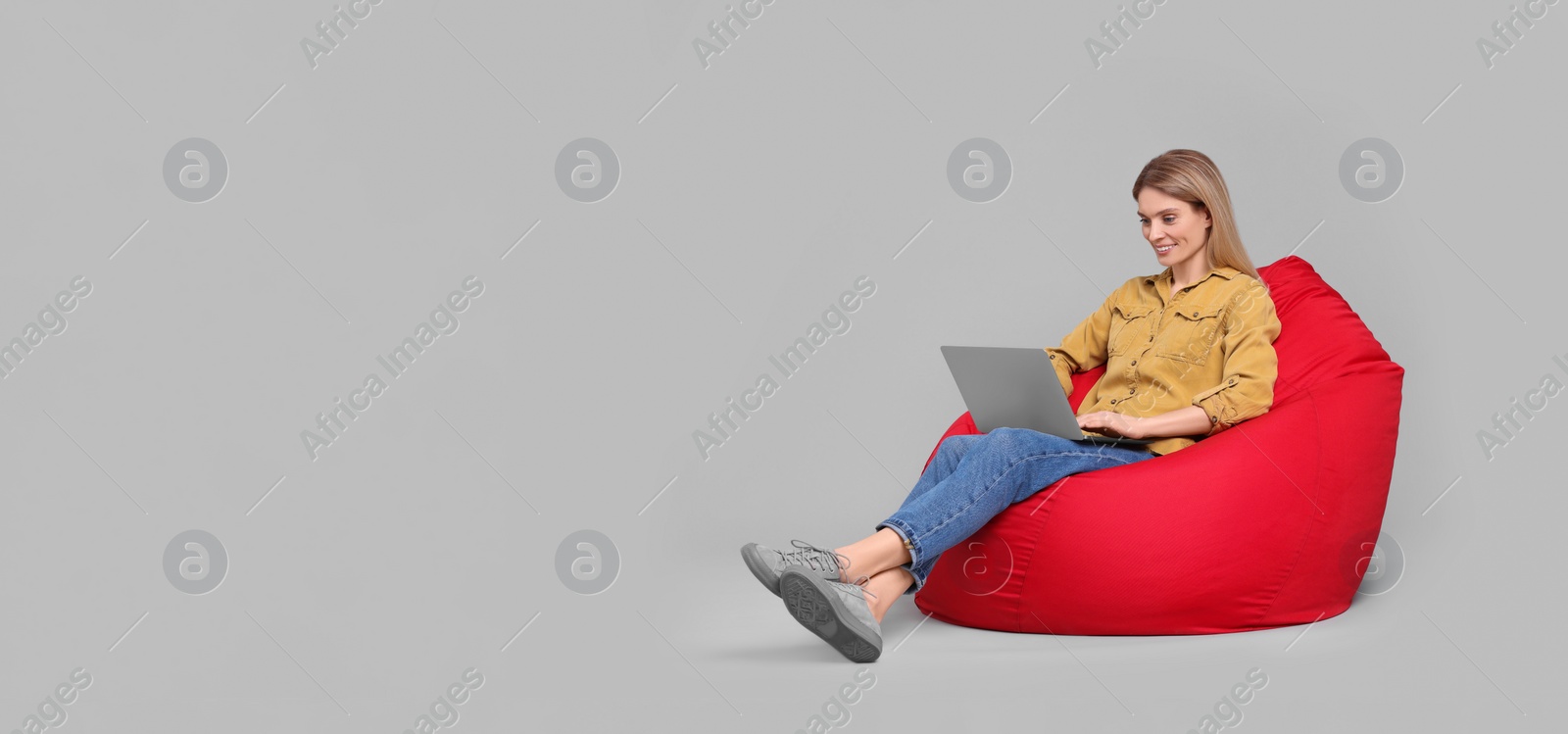 Photo of Happy woman with laptop sitting on beanbag chair against light grey background