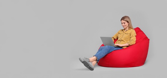 Happy woman with laptop sitting on beanbag chair against light grey background