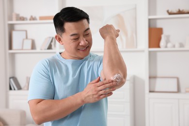 Photo of Handsome man applying body cream onto his elbow at home