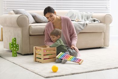 Young nanny and cute little baby playing with toys at home