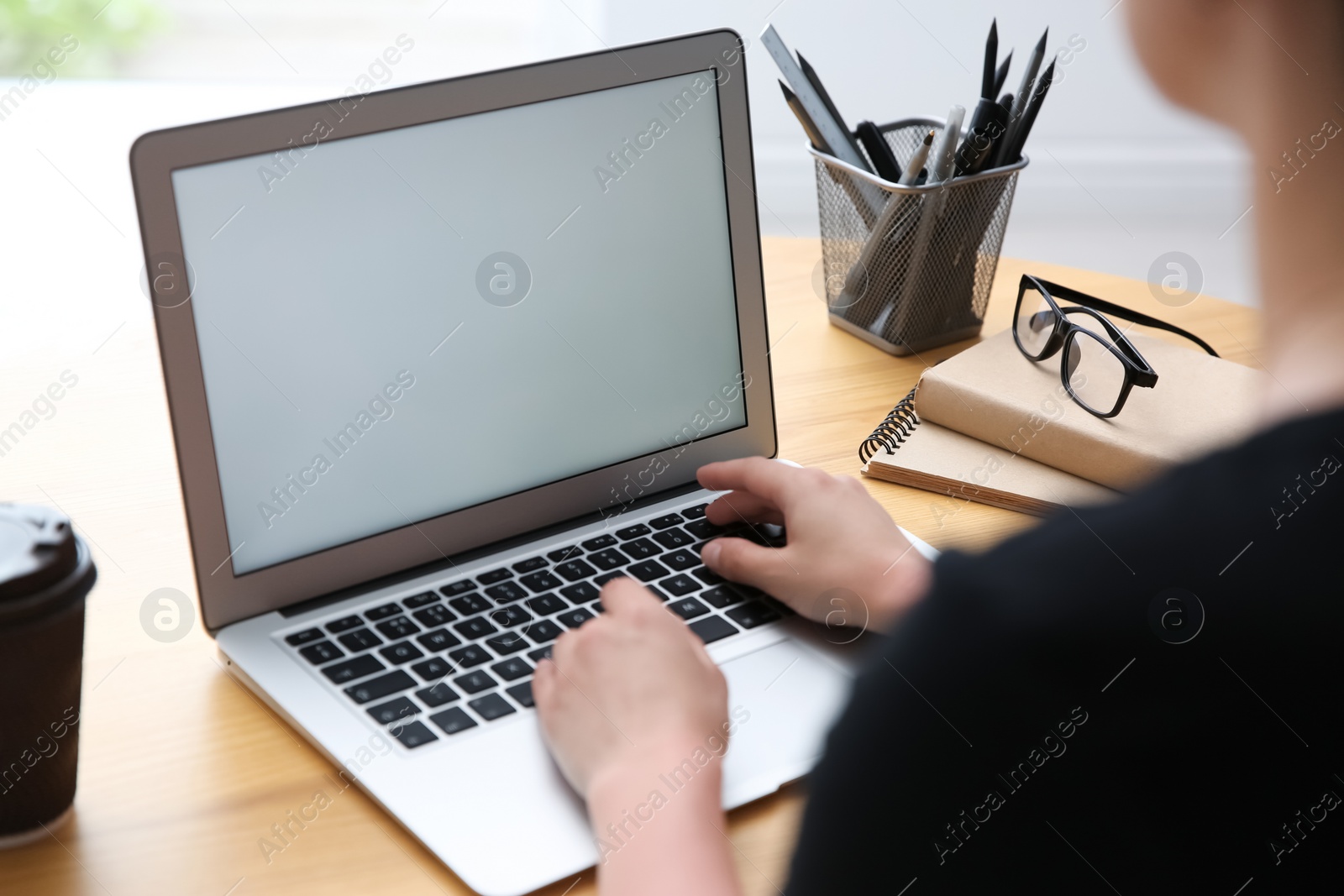 Photo of Woman working with modern laptop at wooden table, closeup. Space for design