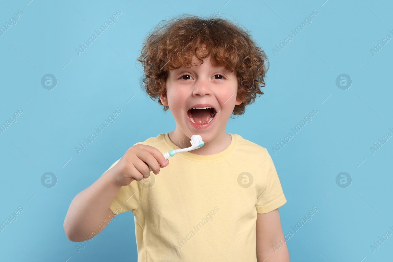 Photo of Cute little boy holding plastic toothbrush on light blue background