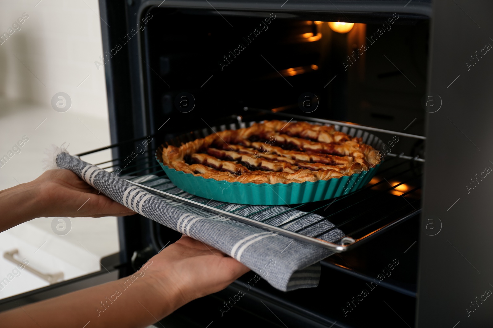 Photo of Woman taking delicious fresh homemade cake out of oven indoors, closeup