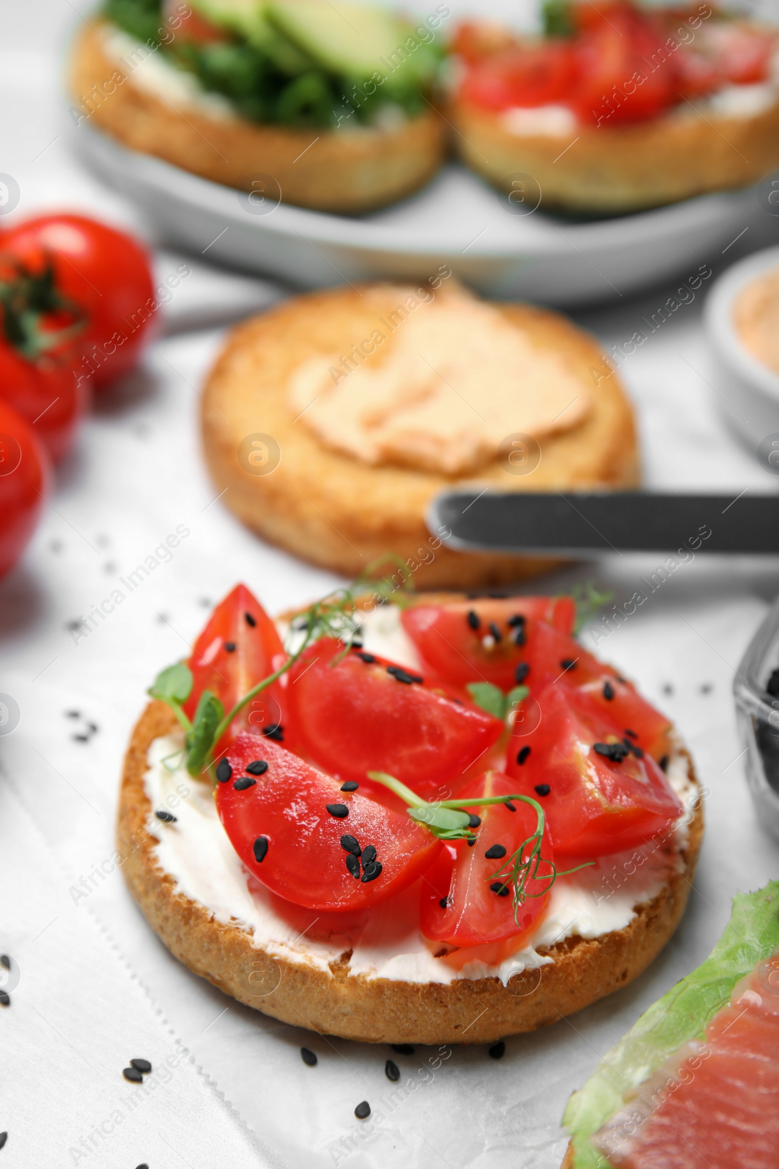 Photo of Tasty rusk with cream cheese, fresh tomatoes and black sesame seeds on white table, closeup