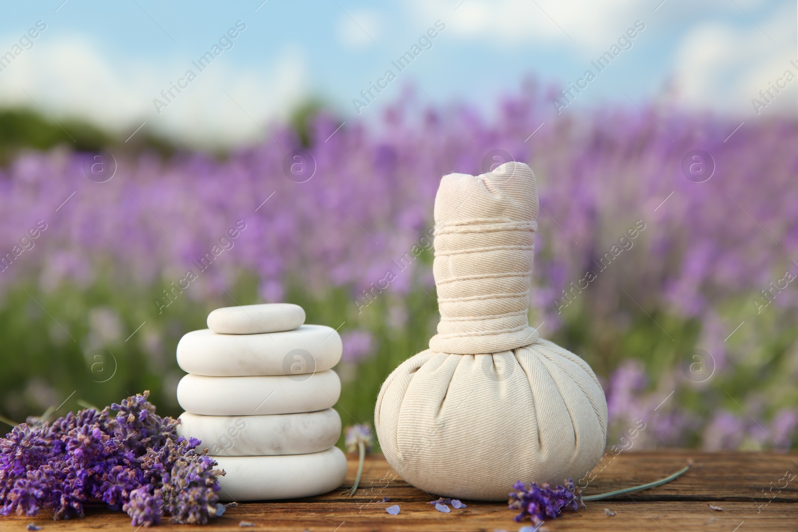 Photo of Spa stones, fresh lavender flowers and herbal bag on wooden table outdoors, closeup