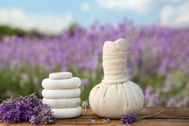 Photo of Spa stones, fresh lavender flowers and herbal bag on wooden table outdoors, closeup