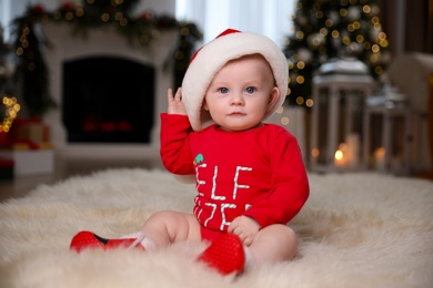 Cute little baby in red bodysuit and Santa hat on floor at home. Christmas suit