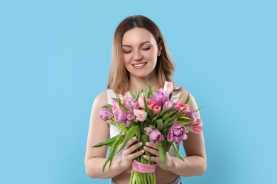 Happy young woman with bouquet of beautiful tulips on light blue background