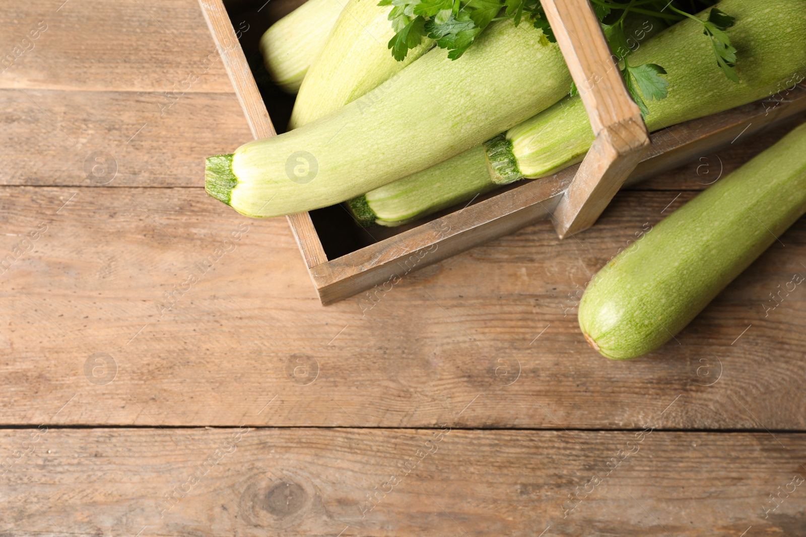 Photo of Crate with ripe zucchinis on wooden table, flat lay. Space for text