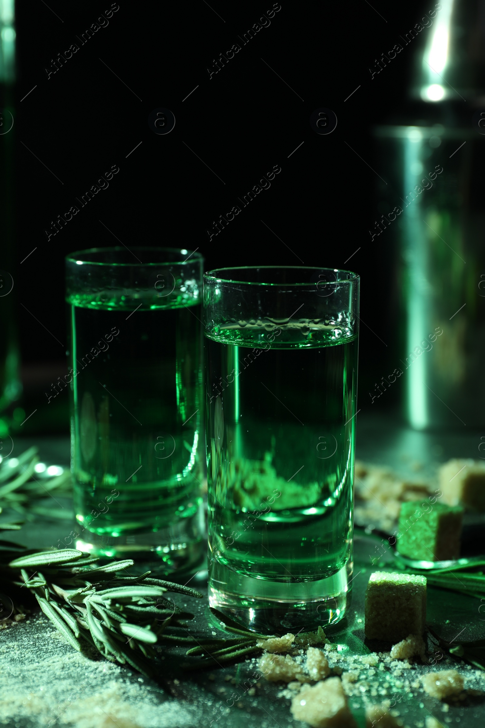 Photo of Absinthe in shot glasses, rosemary and brown sugar on table, closeup. Alcoholic drink