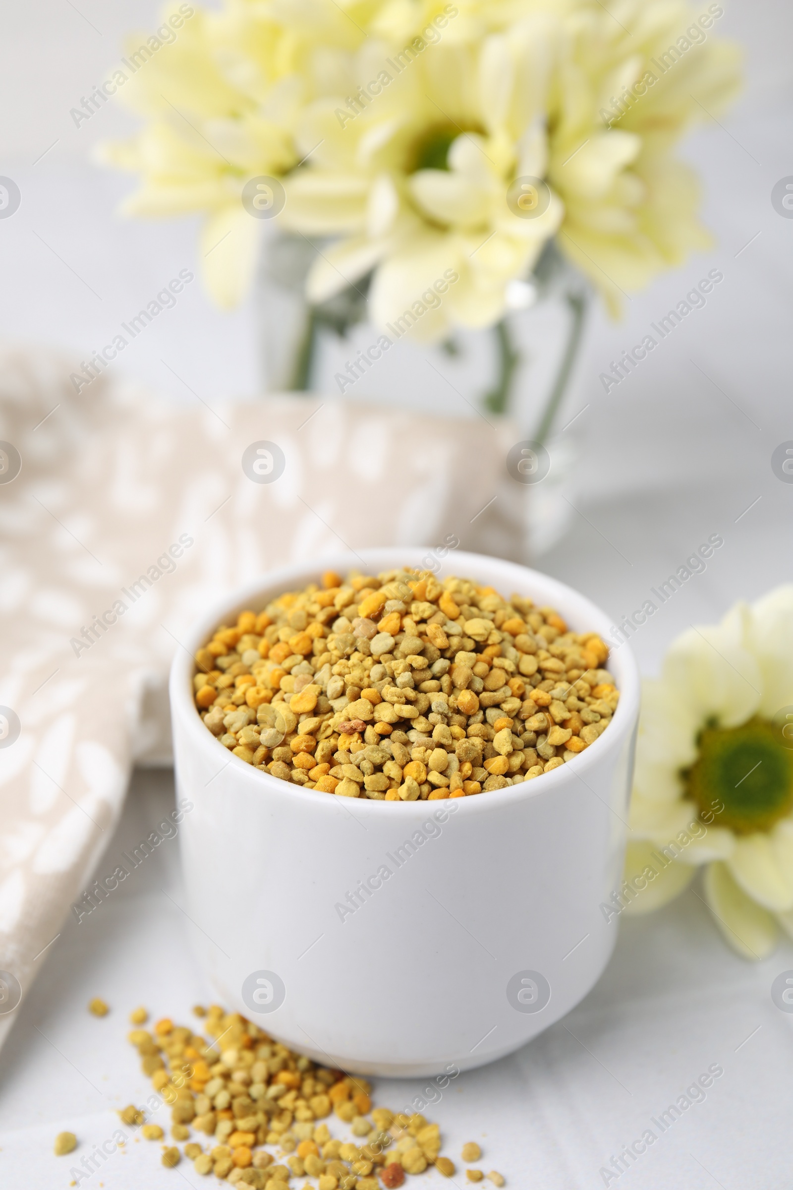 Photo of Fresh bee pollen granules and flowers on white tiled table, closeup